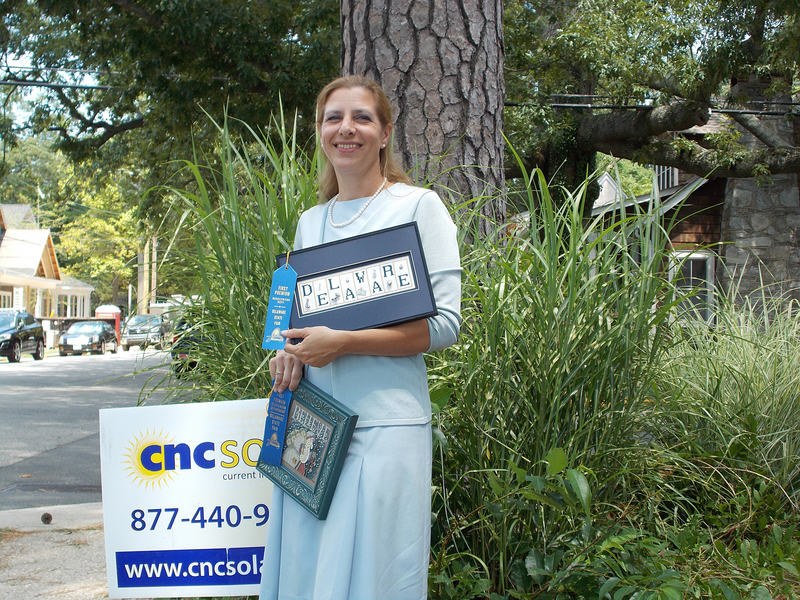 Nancy Moore, who works for CNC Solar in Rehoboth Beach, shows off two of her first-prize cross-stitch pieces. BY RACHEL SWICK MAVITY
